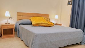 Cama bem arrumada com colcha cinza, um travesseiro amarelo e duas mesas de cabeceira com abajures.