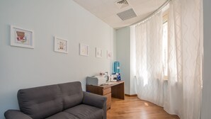 Een kamer met een grijze bank, een bureau met een printer, en ingelijste foto’s aan de muur.