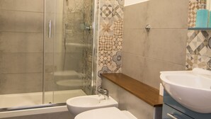 Een badkamer met een glazen douchecabine, toilet, bidet en wastafel.