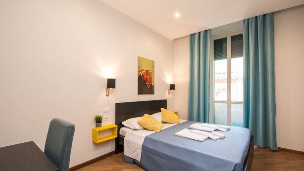 Hotelkamer met een bed, nachtkastjes, een stoel, een kleine plant en een raam met gordijnen.