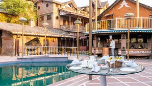 Una zona de piscina con comedor y un edificio de arquitectura tradicional.