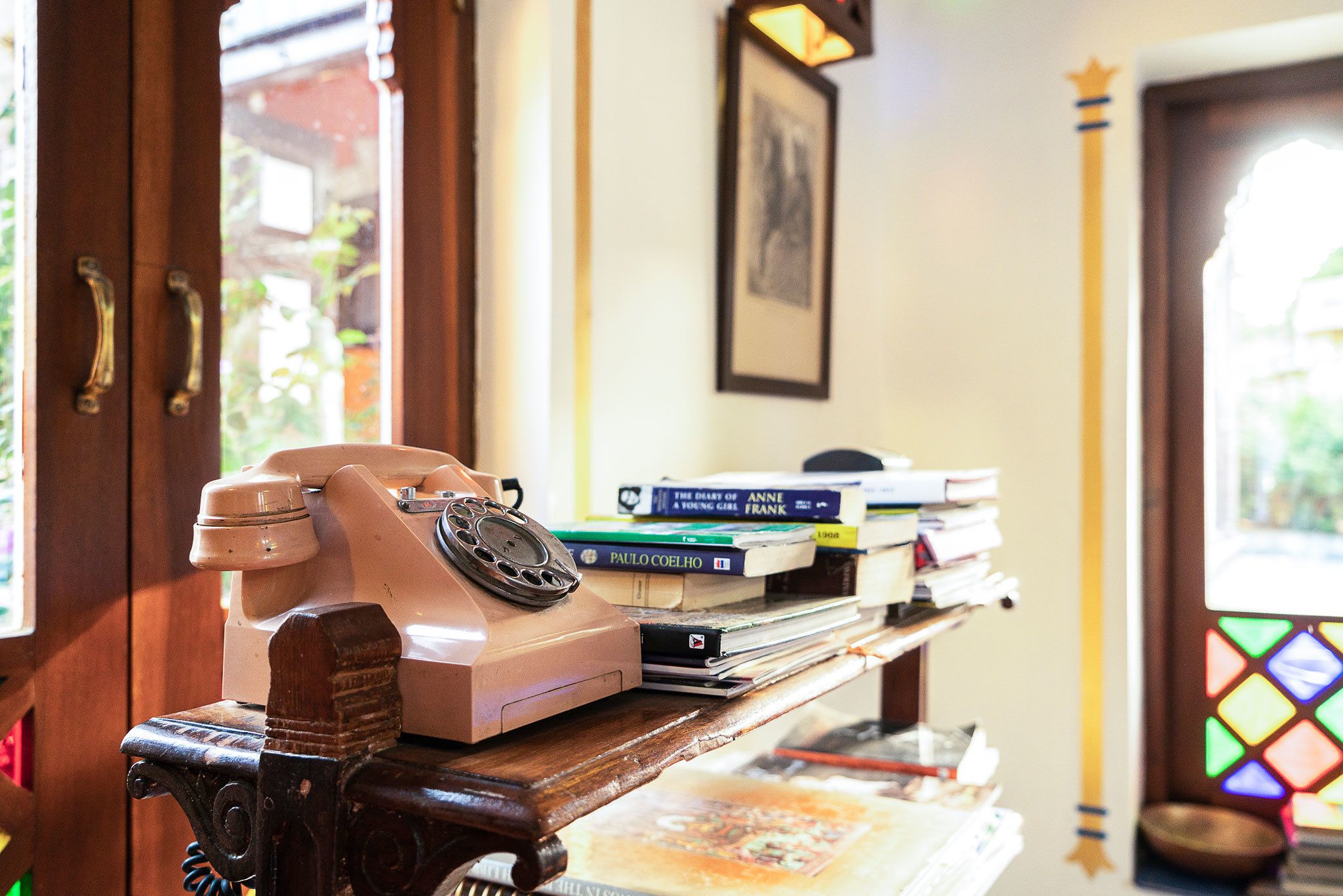 A vintage rotary phone on a wooden desk with books and a framed picture on the wall.