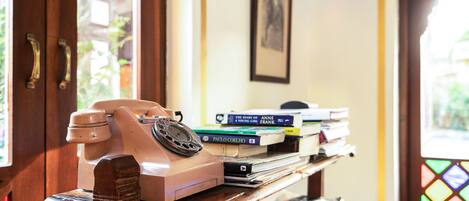 A vintage rotary phone on a wooden desk with books and a framed picture on the wall.