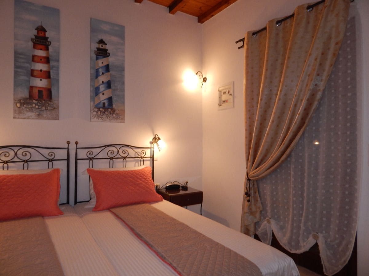 A bedroom with a bed, two pillows, a nightstand, a lamp, and two paintings of lighthouses.