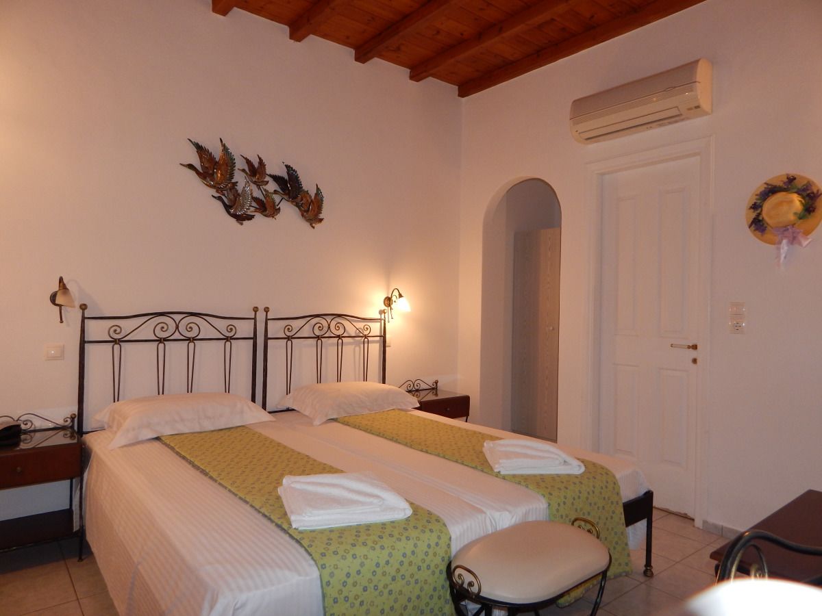 Una cama doble con cabecera, dos mesitas de noche, un banco y una puerta con arco.