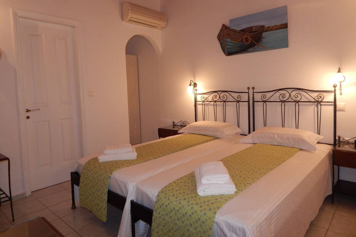 Une chambre avec deux lits, une porte, un appareil de climatisation, un tableau et une lampe.