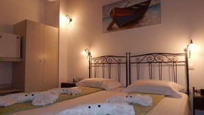 Habitación de hotel con dos camas, cada una con toallas ordenadamente dobladas y una colcha estampada en tonos verdes. Se observa un cuadro de un barco en la pared, y un armario de madera.