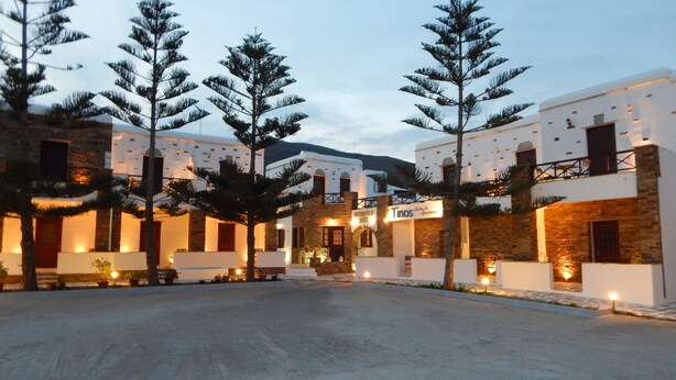 Un patio rodeado de altos pinos, con edificios de fachadas de piedra y color blanco.
