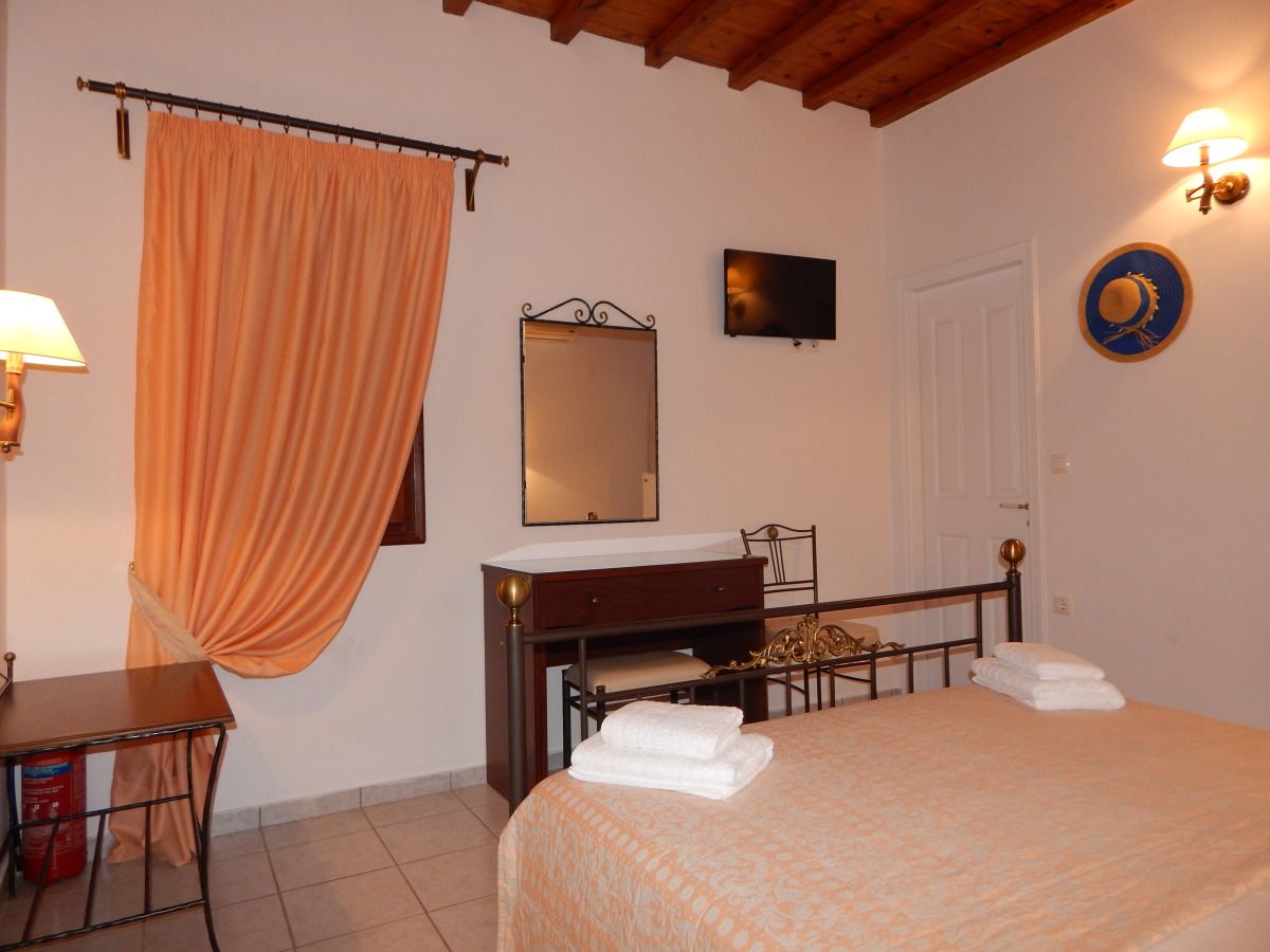 A bedroom with a bed, a desk, a chair, a dresser, a mirror, a wall-mounted TV, and a door.