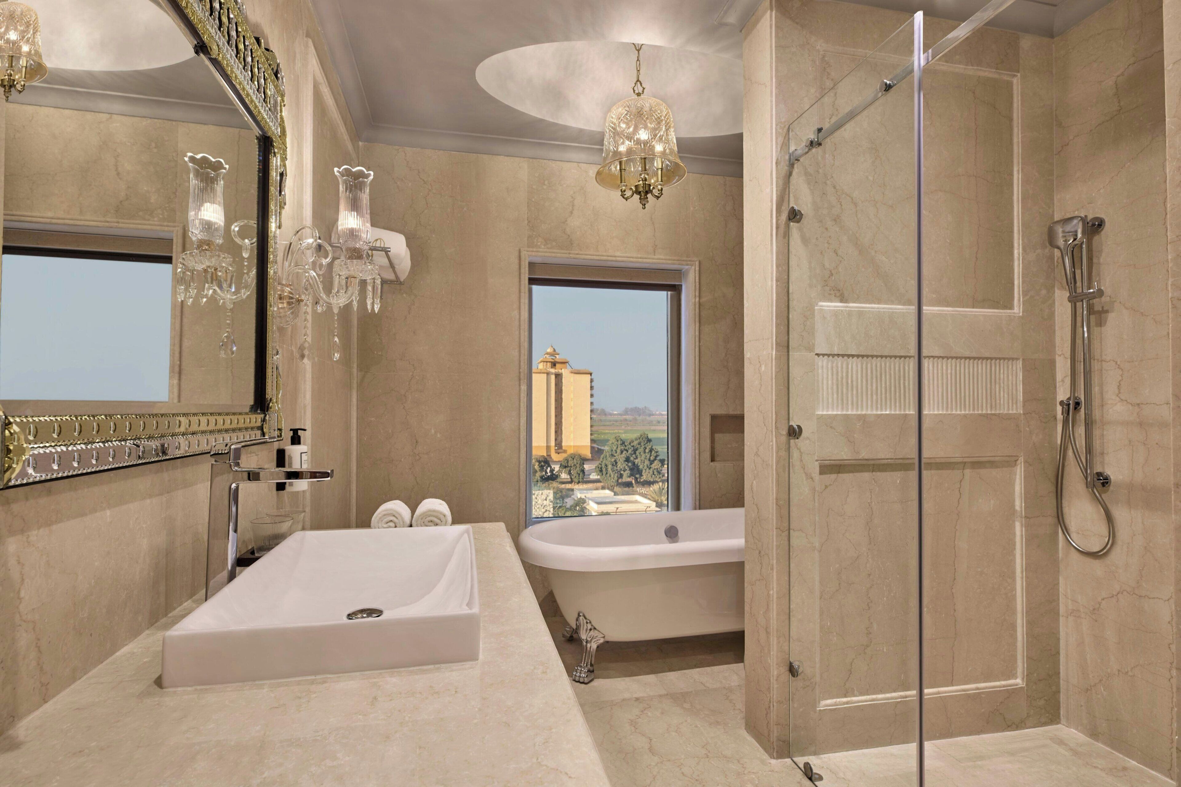 A bathroom with a bathtub, a shower, a large mirror, and a chandelier.