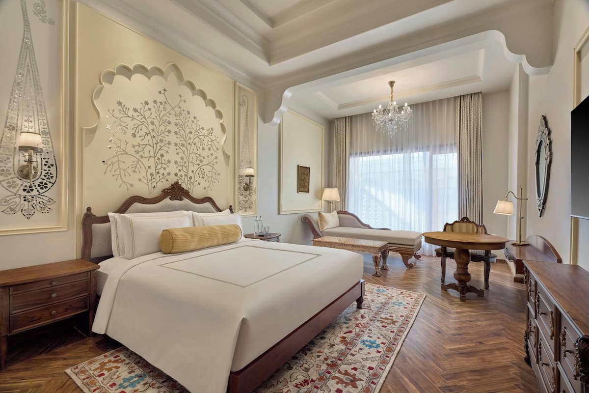 A hotel room with a large bed, a dining table, a chandelier, and a decorative wall panel.