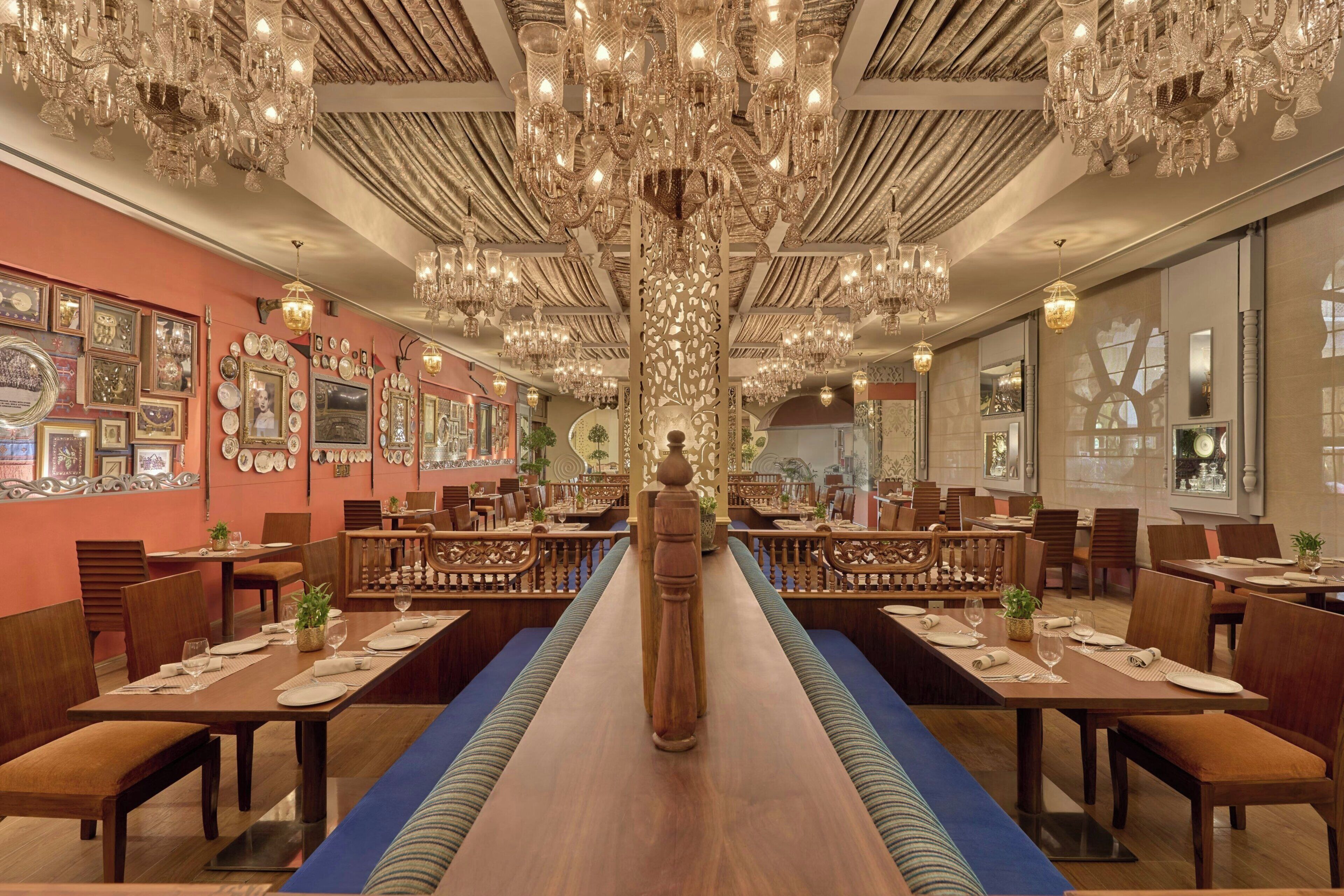 Um restaurante com várias mesas, lustres ornamentados e um pilar decorativo central.