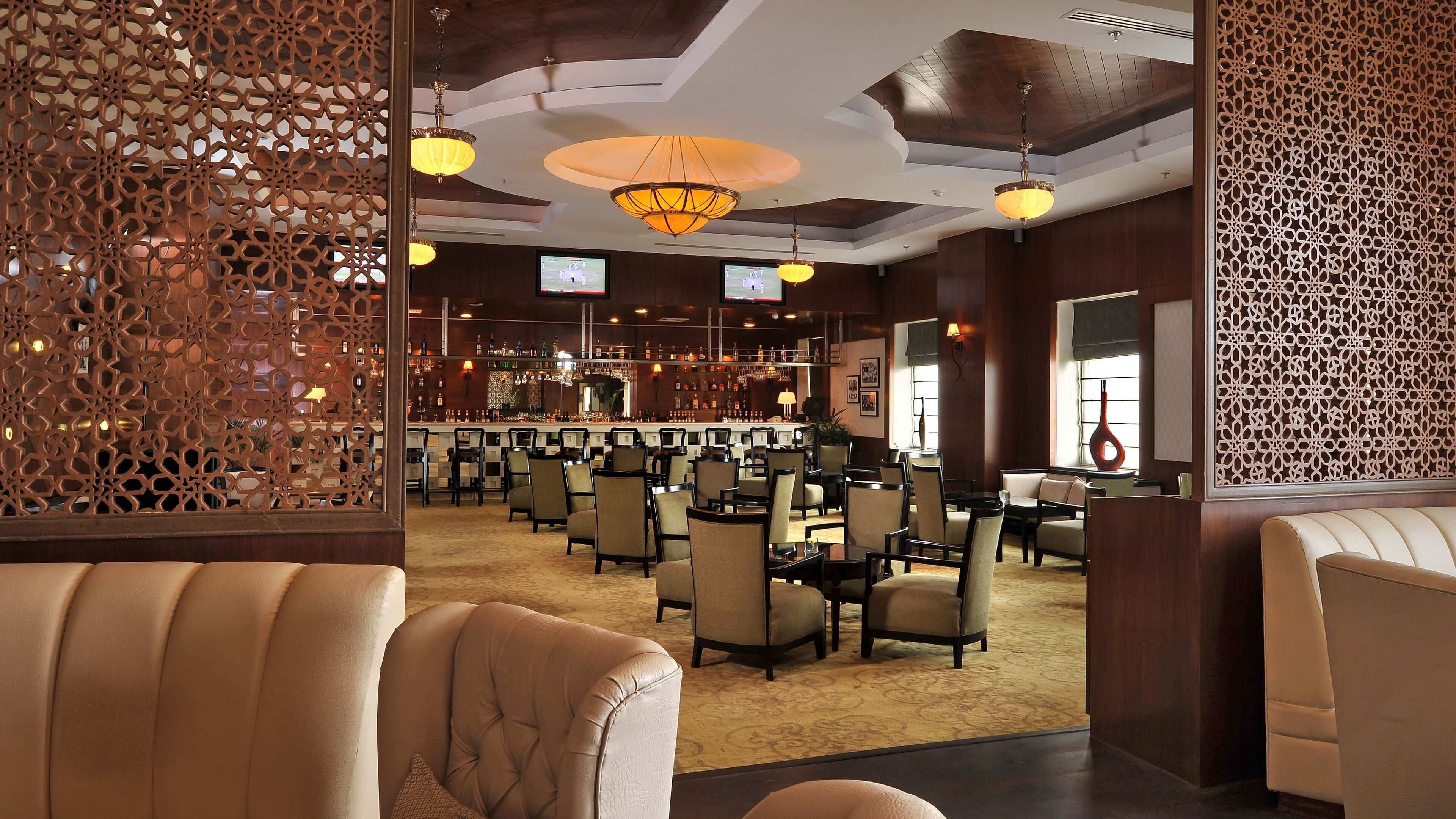 A spacious lounge area with multiple seating arrangements, a bar in the background, and decorative lighting fixtures.