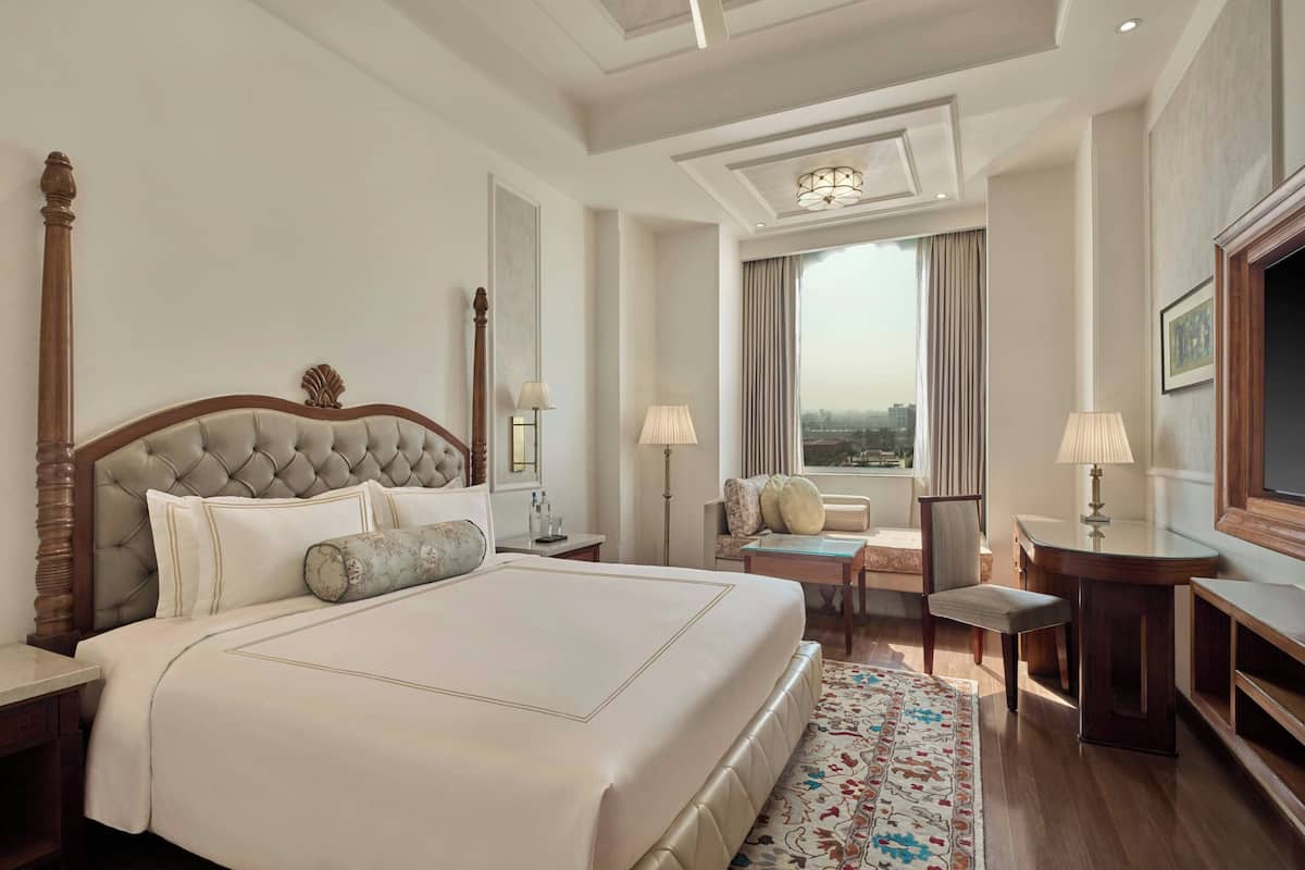 A hotel room with a large bed, a desk, a chair, a television, and a view of the city.