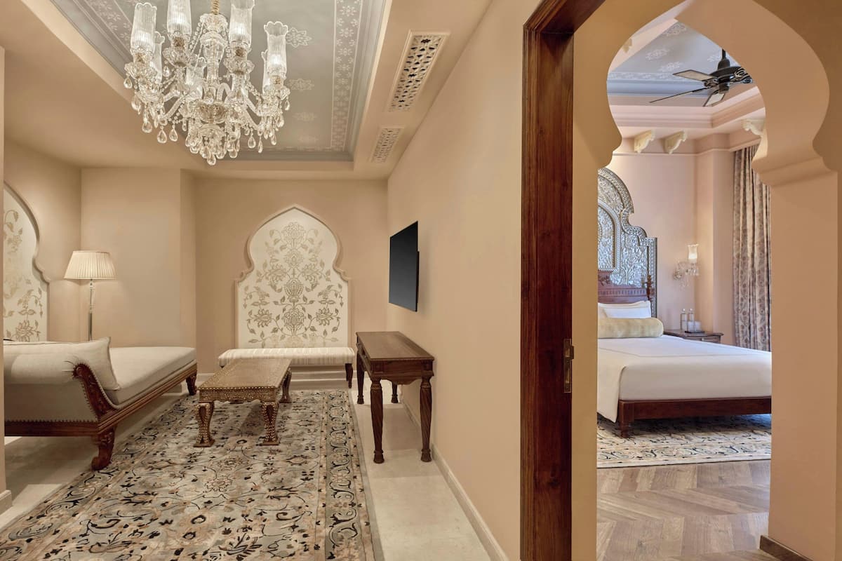 A room with a chandelier, a patterned rug, a bed, and a wooden bench.