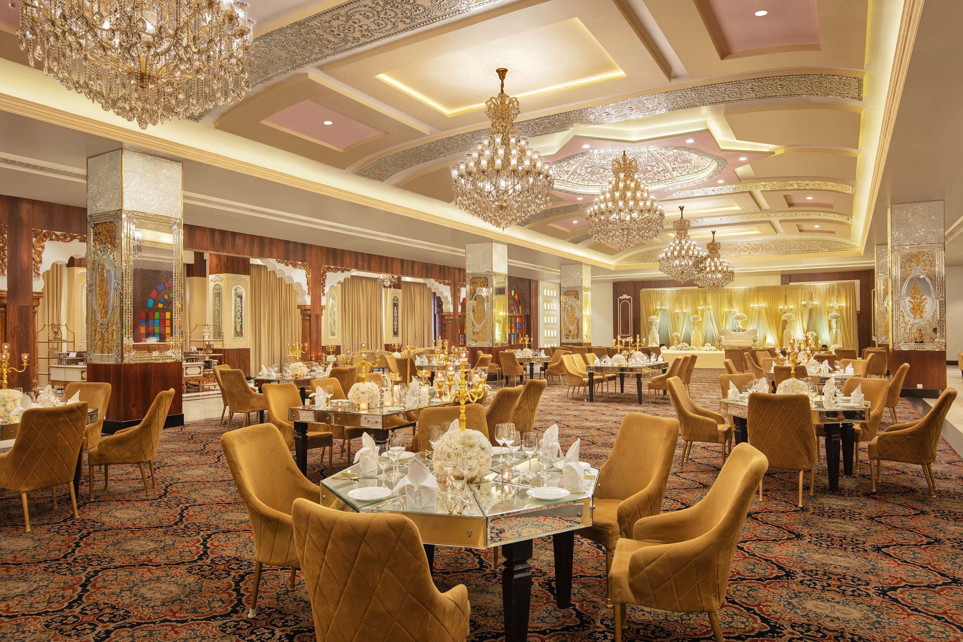 A luxurious banquet hall with ornate chandeliers, gold-toned furniture, and a richly patterned carpet.