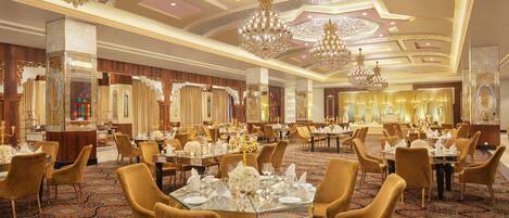A luxurious banquet hall with ornate chandeliers, gold-toned furniture, and a richly patterned carpet.