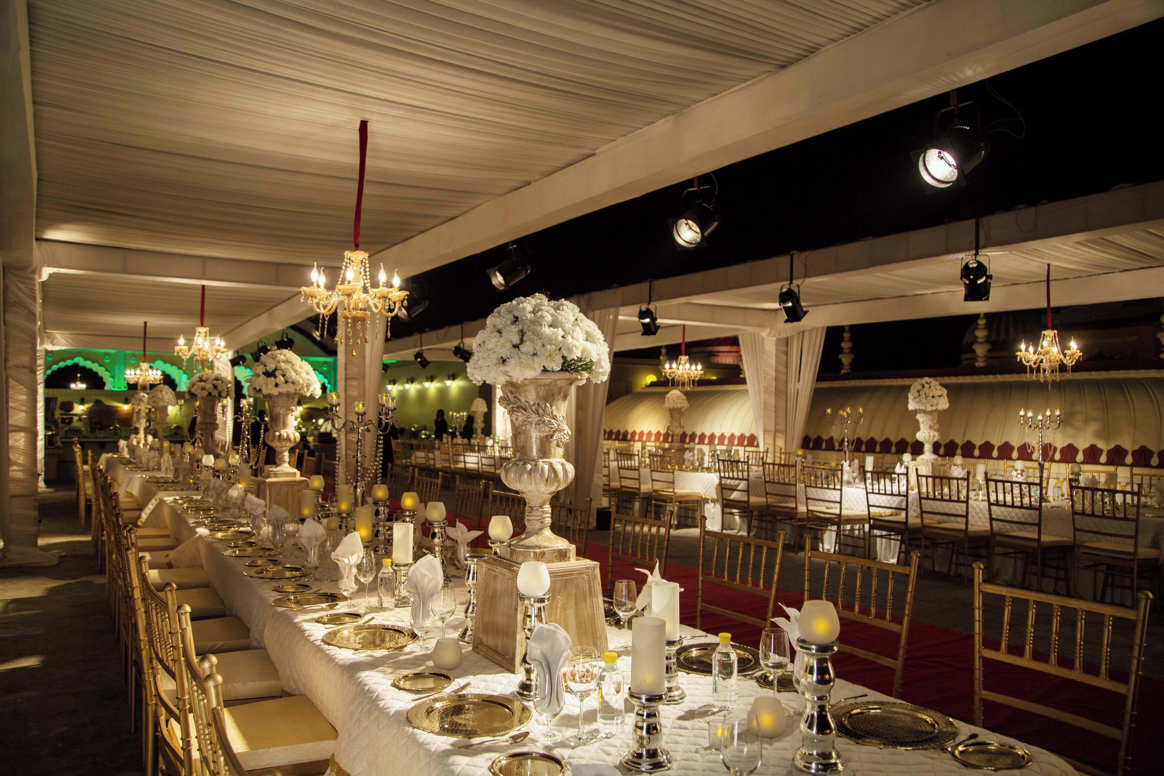 A banquet hall with long tables set for a formal event, featuring chandeliers, floral centerpieces, and elegant table settings.