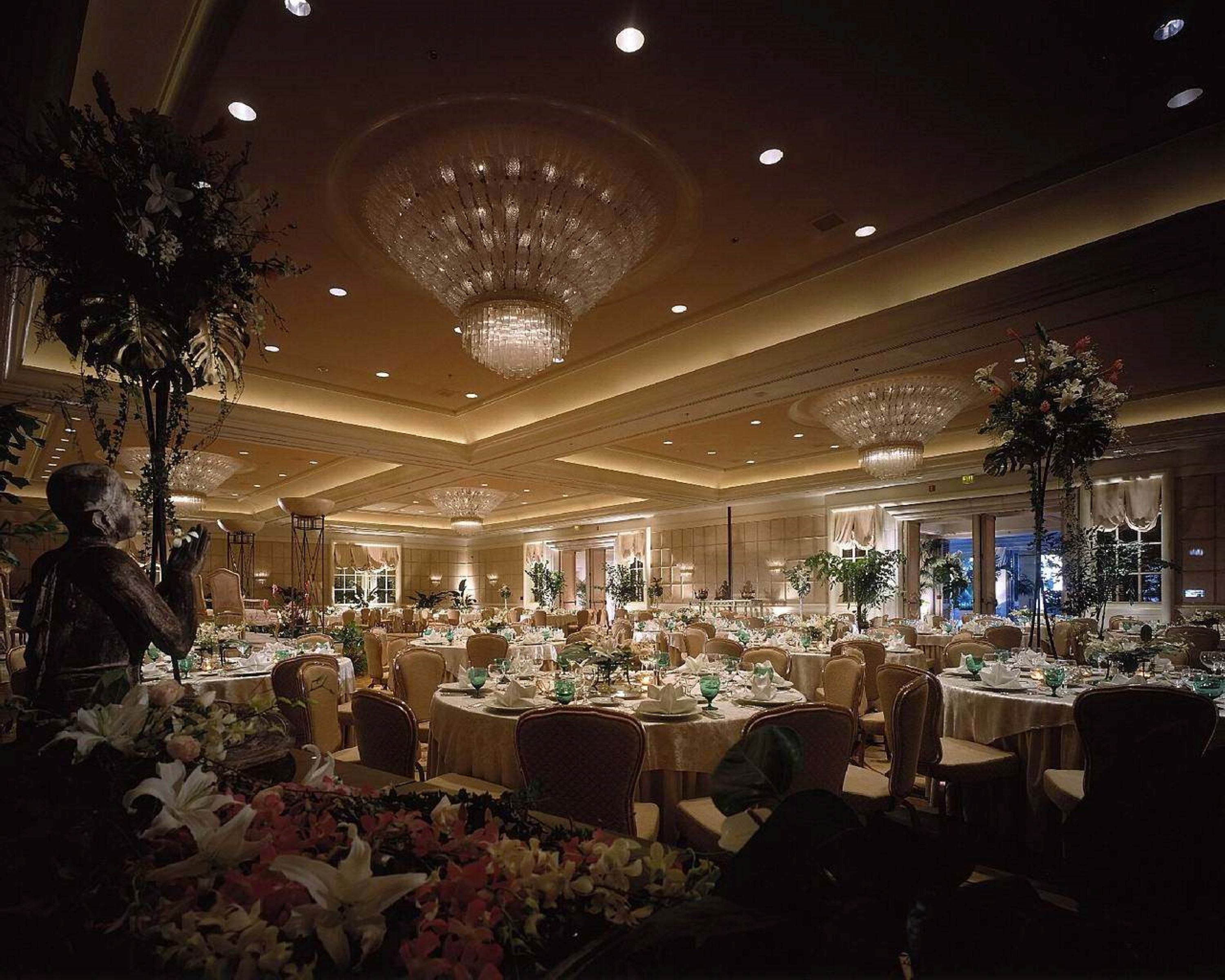 Une salle de banquet avec des tables rondes, des lustres et des compositions florales.