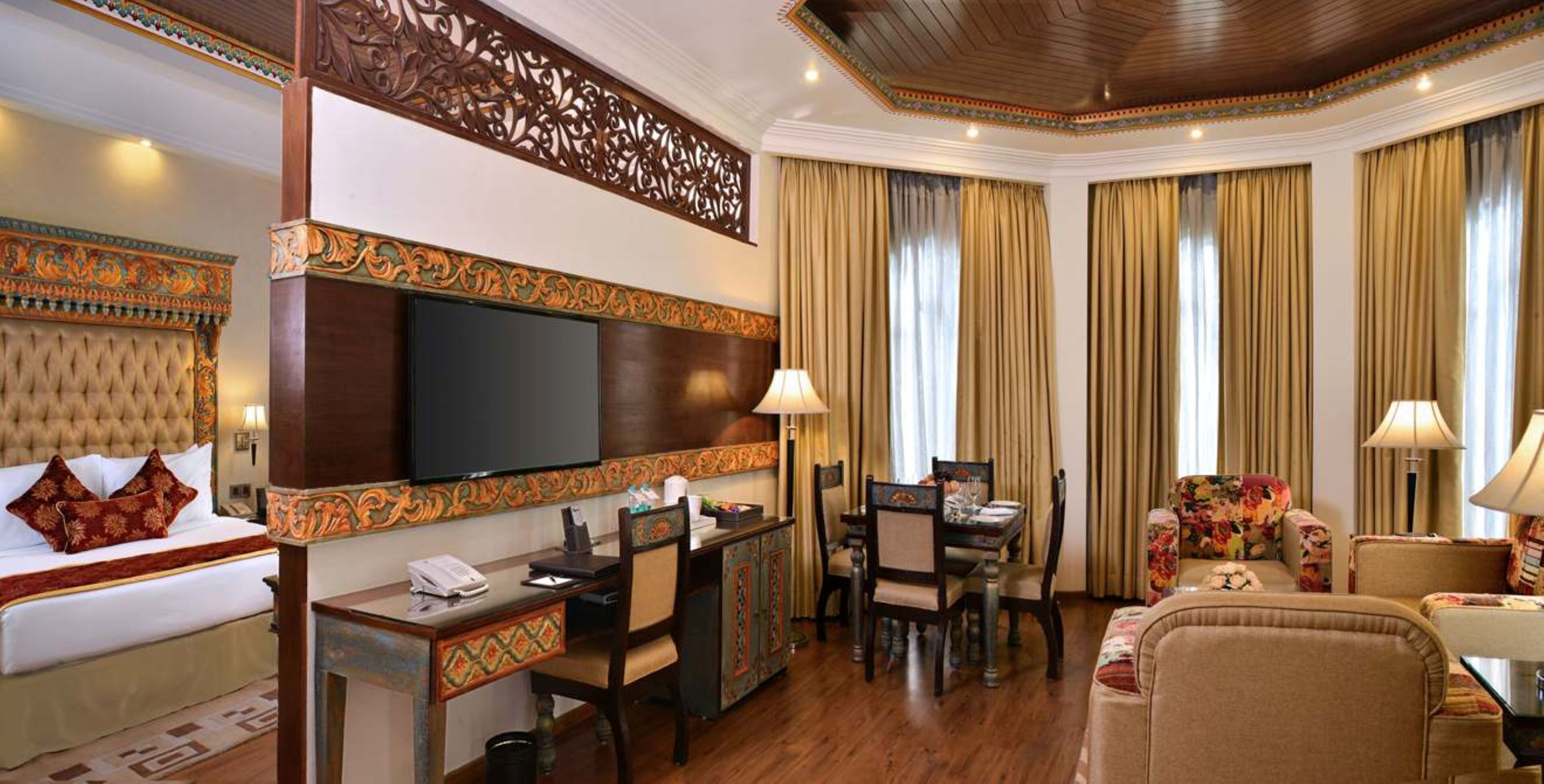 Una habitación de hotel con una cama grande, un escritorio con computadora, un televisor, una zona de comedor con sillas y un sofá.
