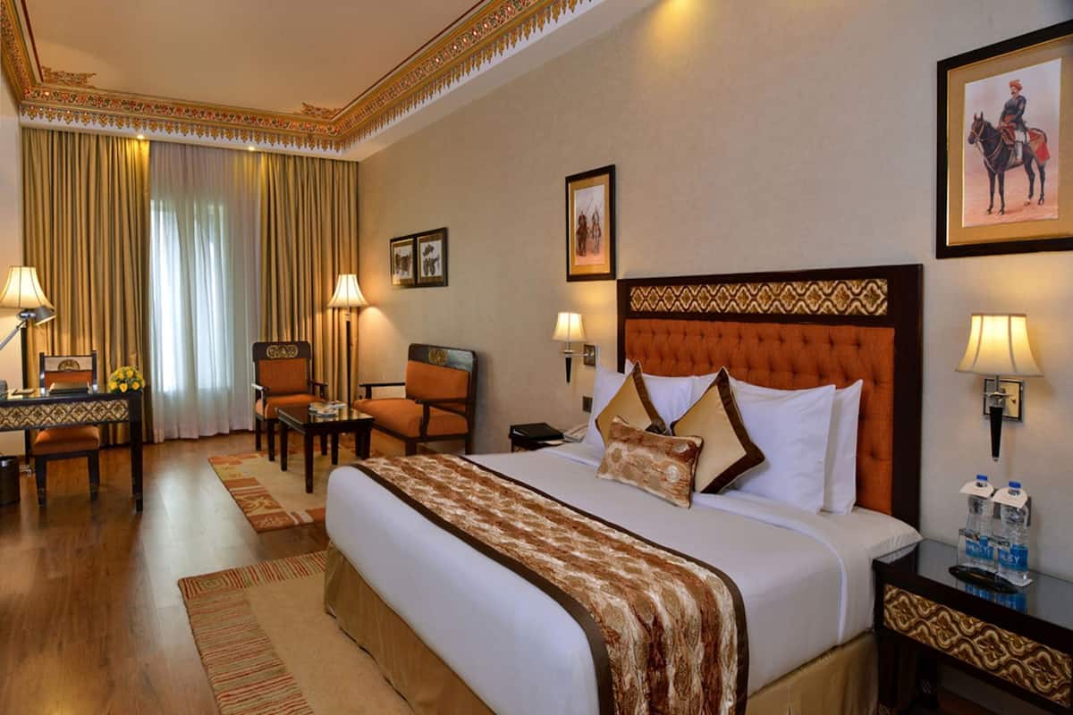 A hotel room with a large bed, two chairs, a desk, a lamp, and a picture on the wall.