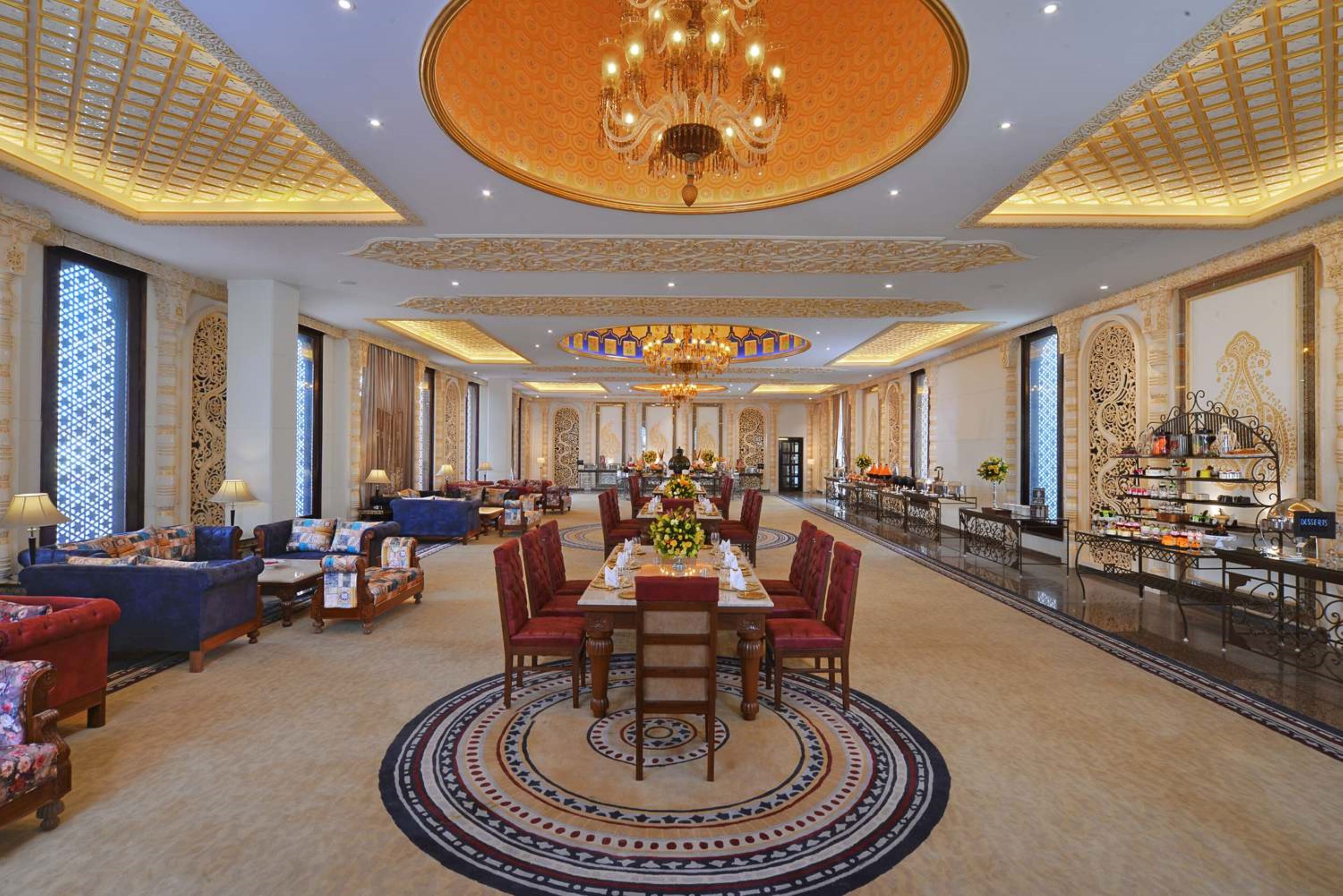 Een luxueuze hotel lobby met een centraal gelegen eetgedeelte, versierde kroonluchters en een hoge plafond.
