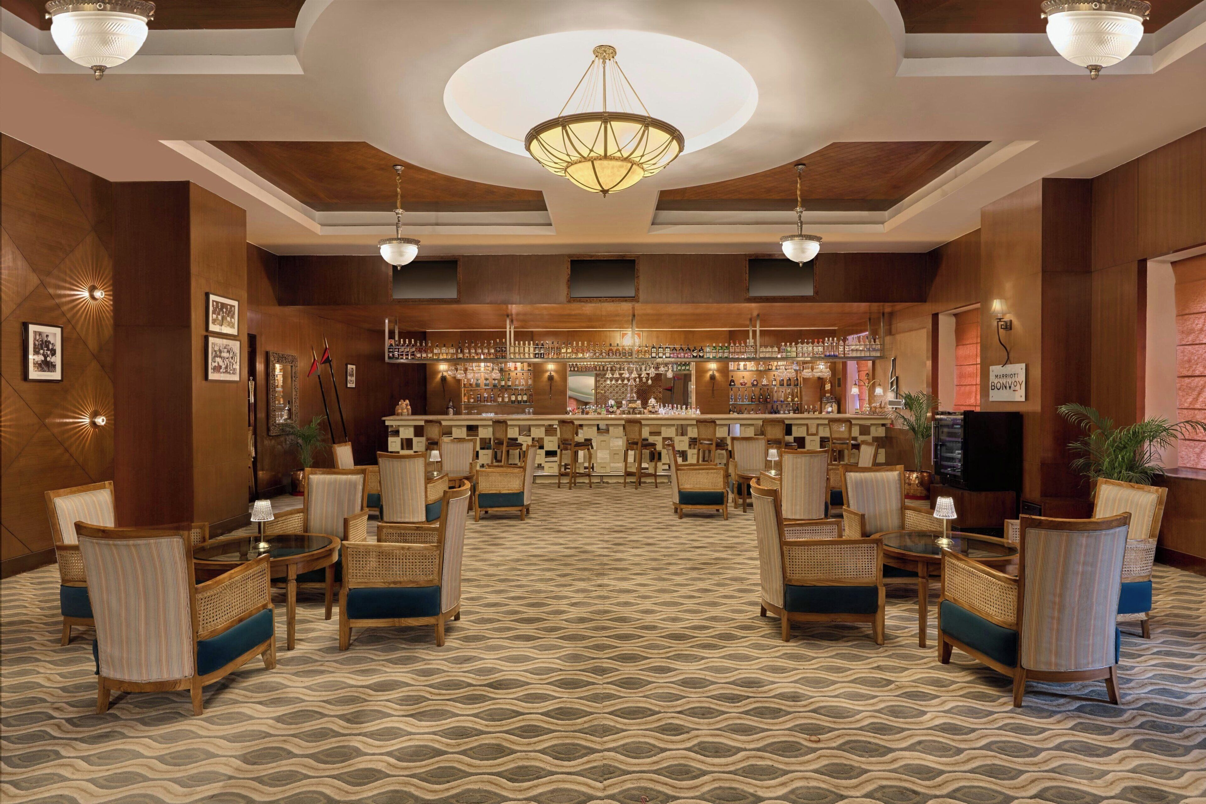 Un vestíbulo de hotel con zona de bar, muebles de mimbre y alfombra estampada.