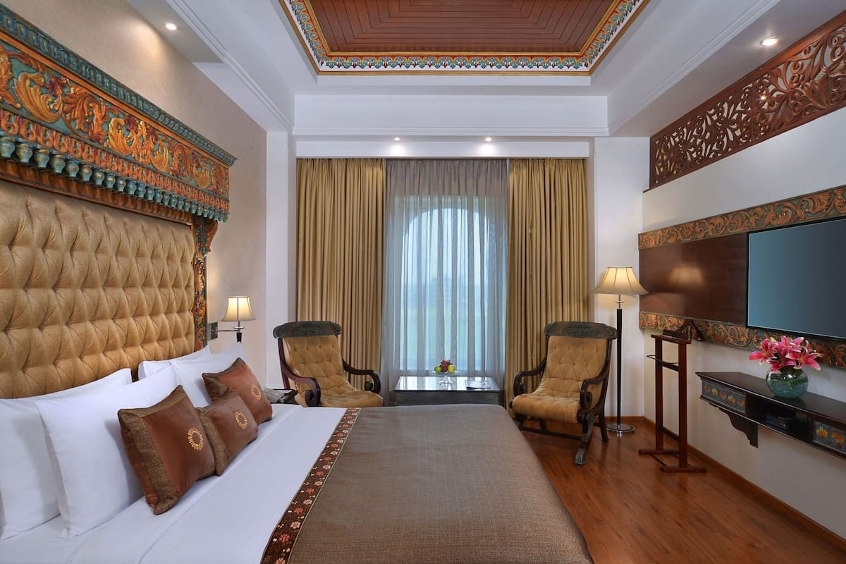 A hotel room with a large bed, two armchairs, a TV, and a decorative ceiling.