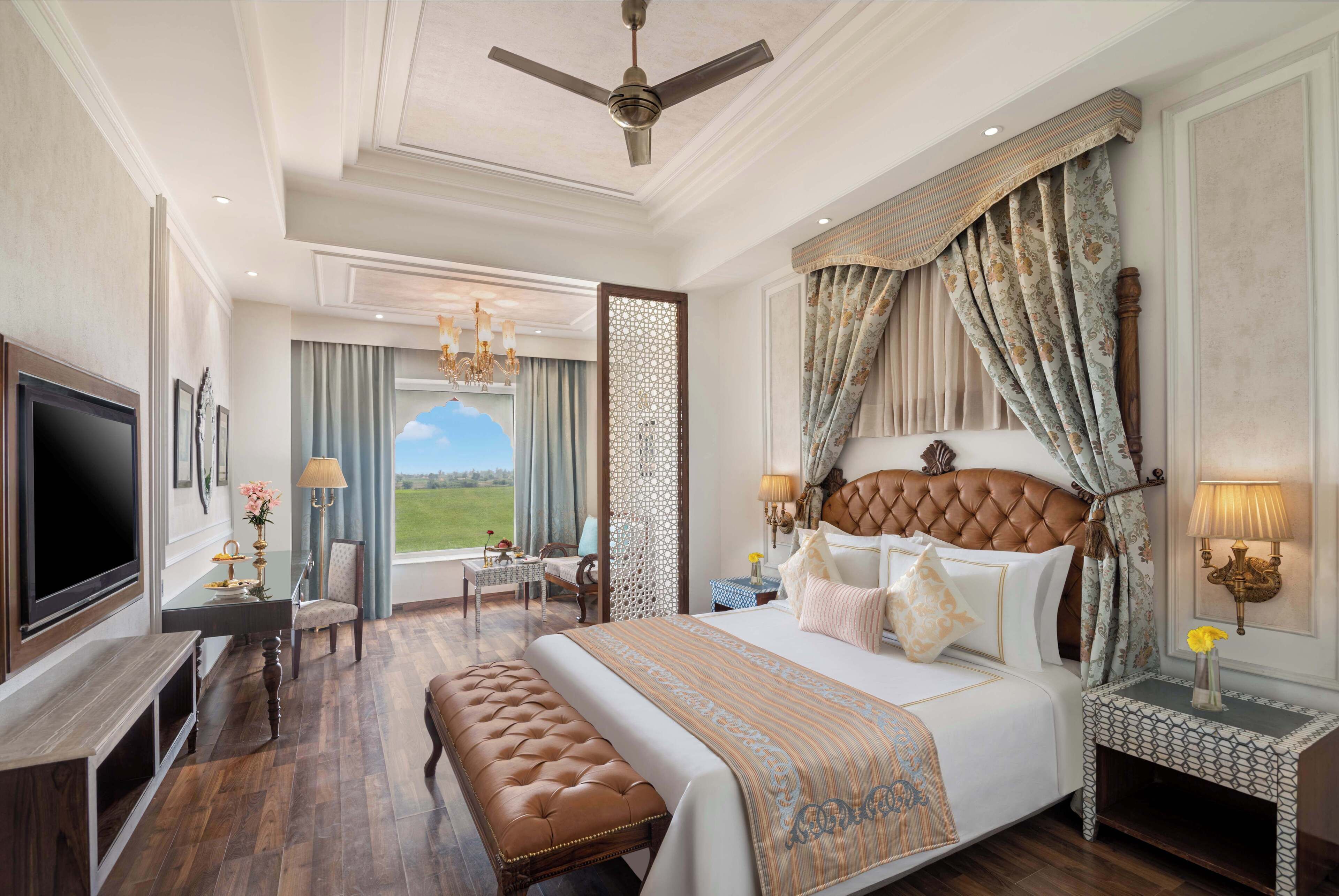 A spacious bedroom with a large bed, a television, a desk, and a view of the outdoors.
