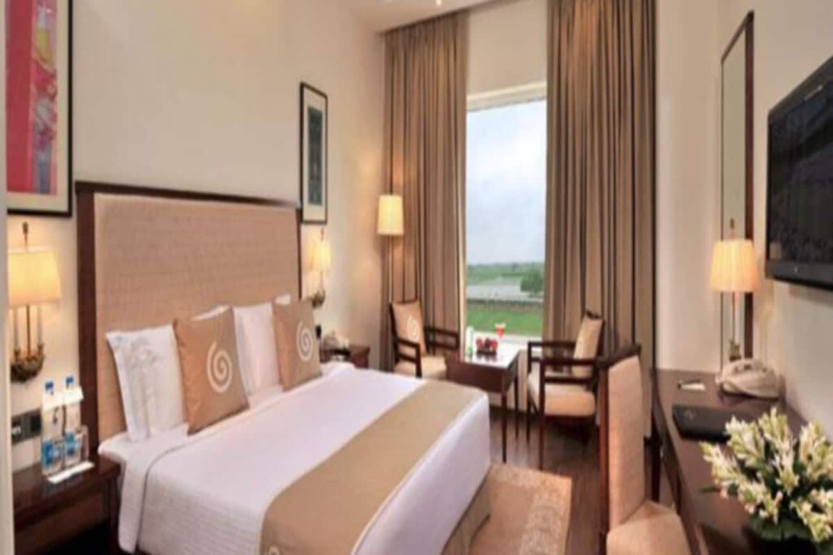 A hotel room with a large bed, two chairs, a desk, a window with curtains, and a view of the outdoors.