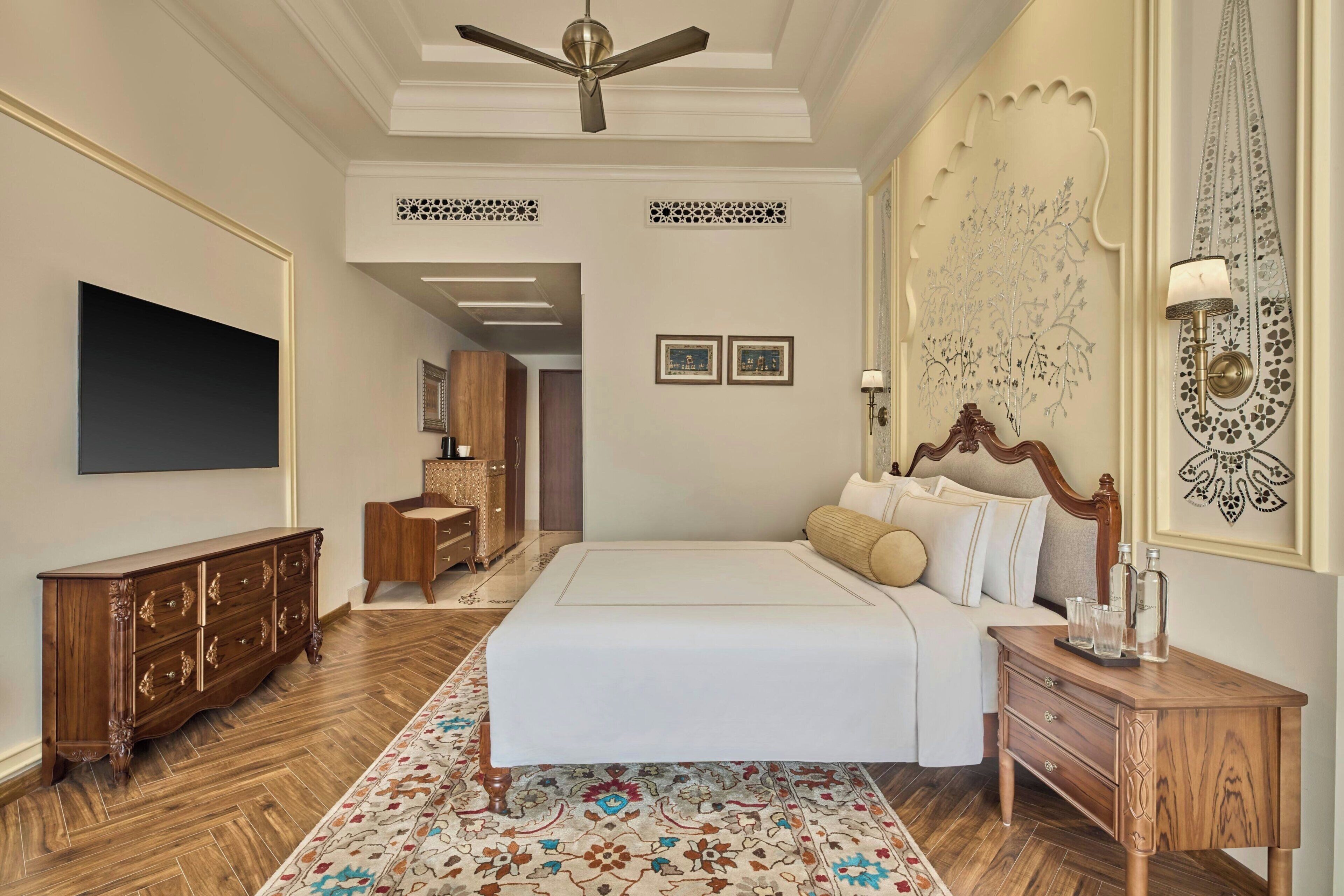 Une chambre à coucher avec un lit, une commode en bois et un téléviseur fixé au mur.