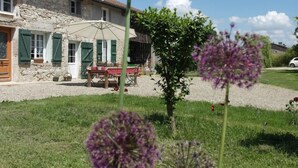 A stone building with a gravel driveway and a table with chairs outside. - Les chambres de Filou (Montesquieu)