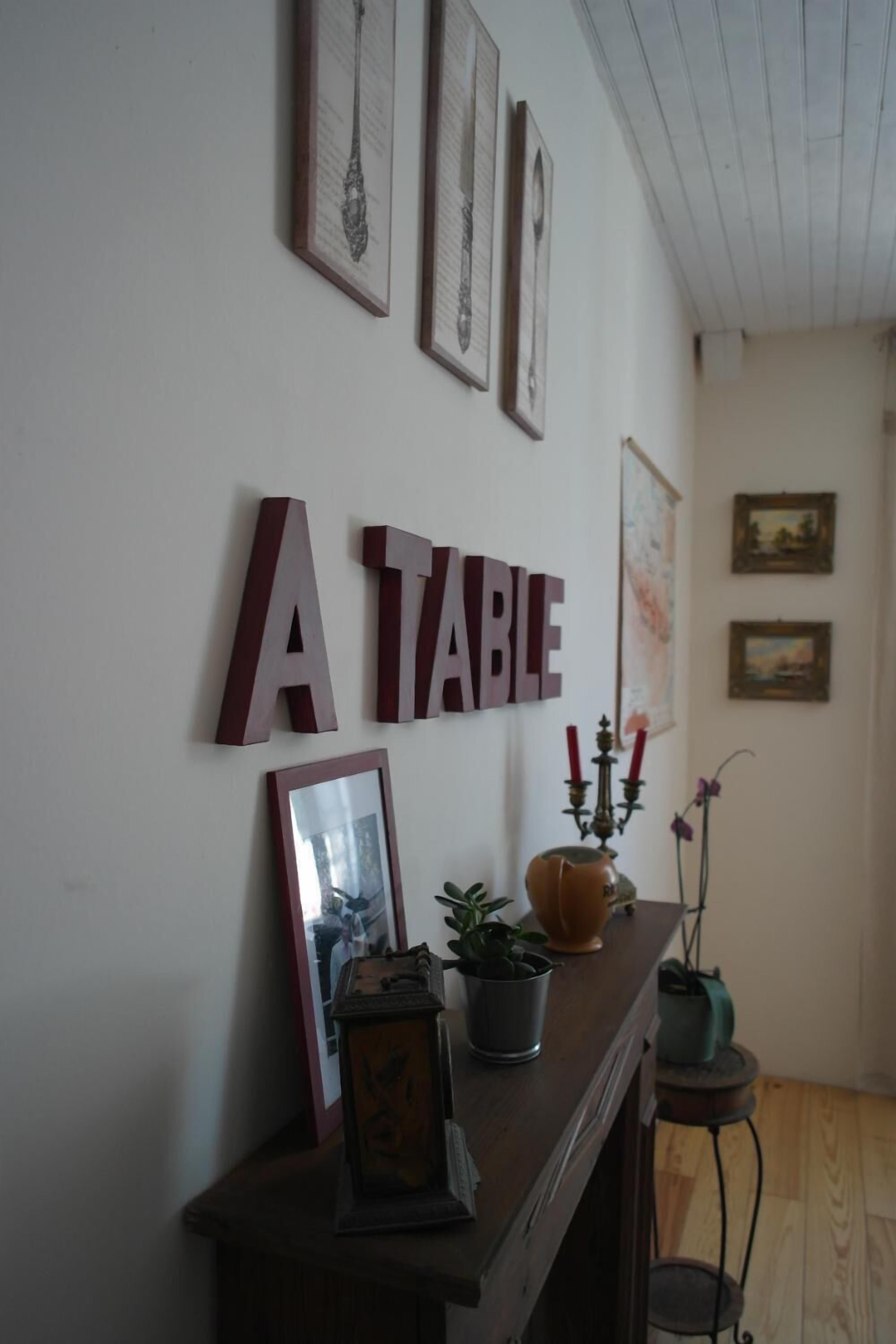 A room with a wooden table, framed pictures on the wall, and a decorative vase with candles.