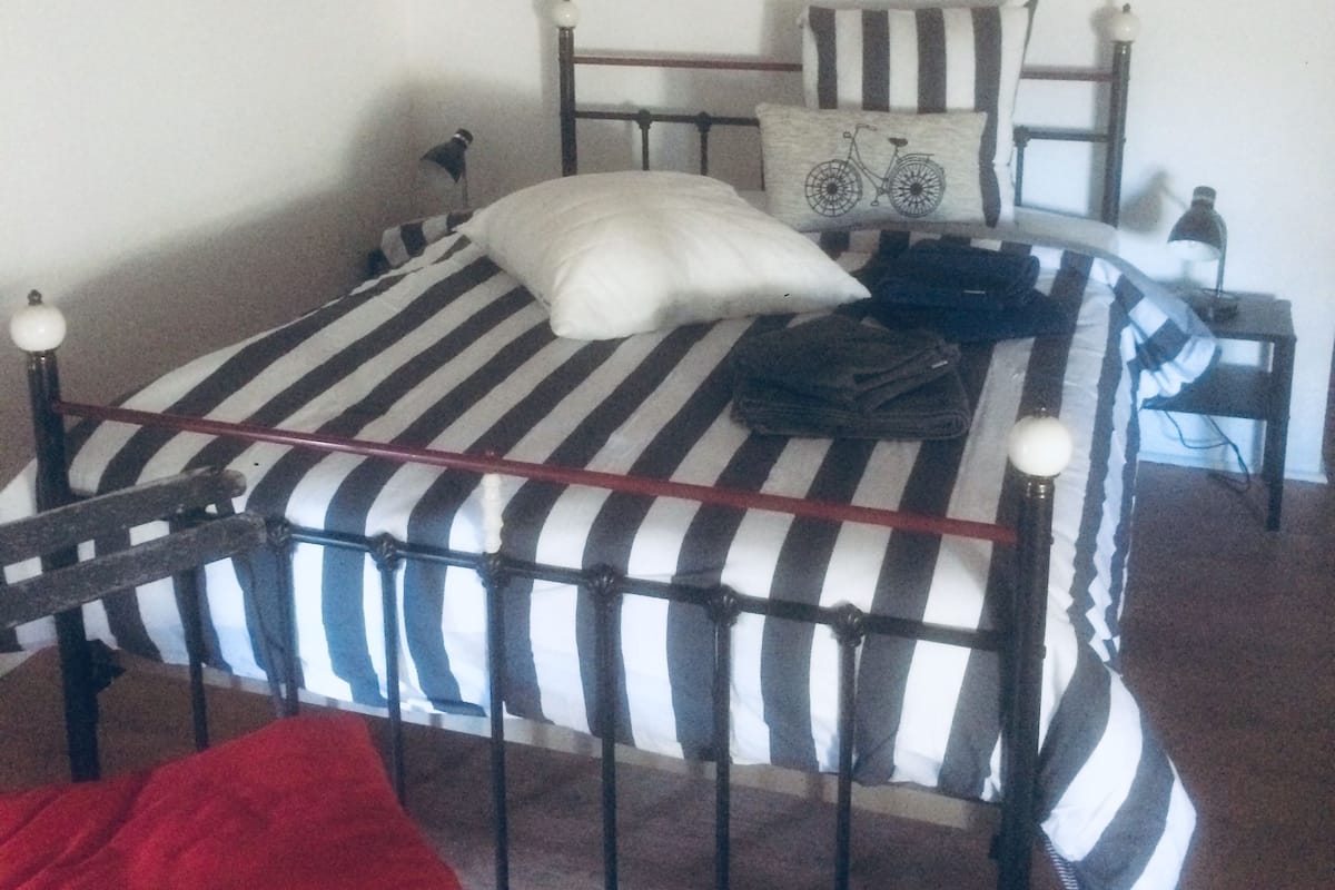 Un dormitorio con una colcha a rayas, una manta roja, una almohada con motivos de bicicleta y un cuadro en la pared.