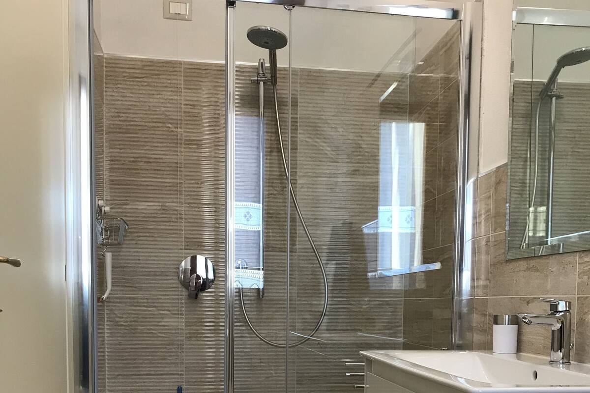 Un baño moderno con ducha de vidrio, un lavabo blanco y un espejo grande.