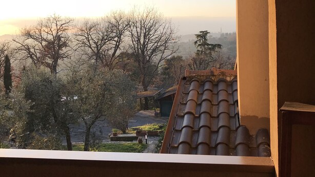 A view through a window with a tiled roof, a stone pathway, and trees. - La Ghirlanda B&B (Arezzo)