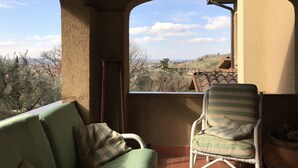 A balcony with a view of a hilly landscape, a green sofa, a striped chair, and a potted plant. - La Ghirlanda B&B (Arezzo)
