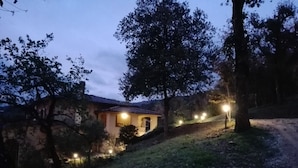 A stone house with a tiled roof, surrounded by trees and a grassy slope. - La Ghirlanda B&B (Arezzo)