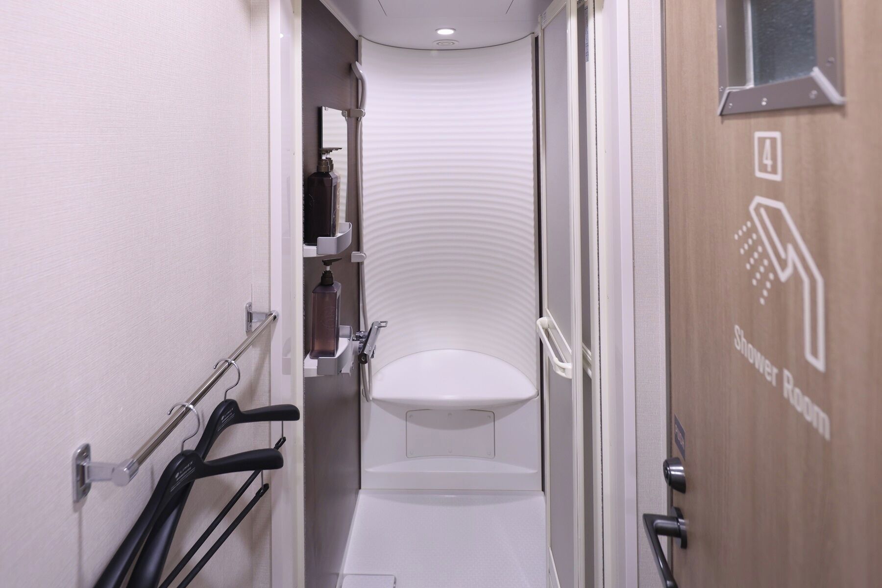 A narrow, modern bathroom with a white toilet, a shower area, and a handrail on the left.