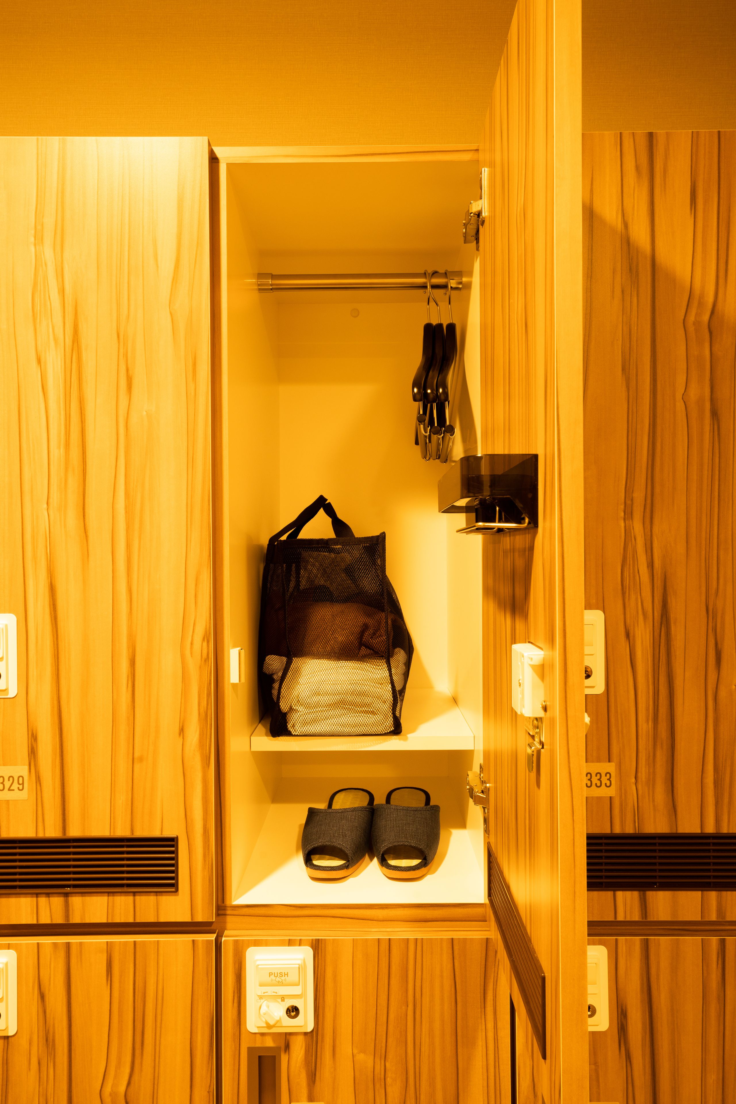 Un armario de madera con un zapatero colgante, un estante con un bolso y sandalias, y una luz con pulsador.