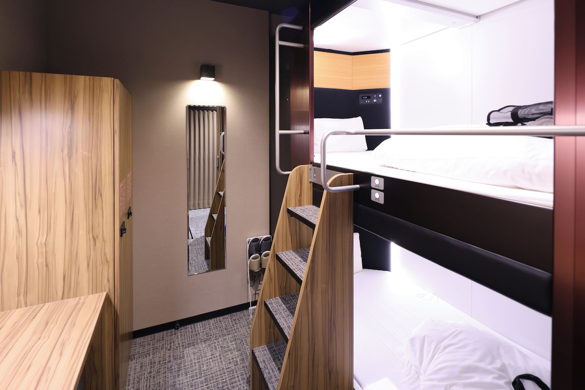 Habitación de hotel pequeña con una cama litera, un armario de madera, un escritorio y un espejo.