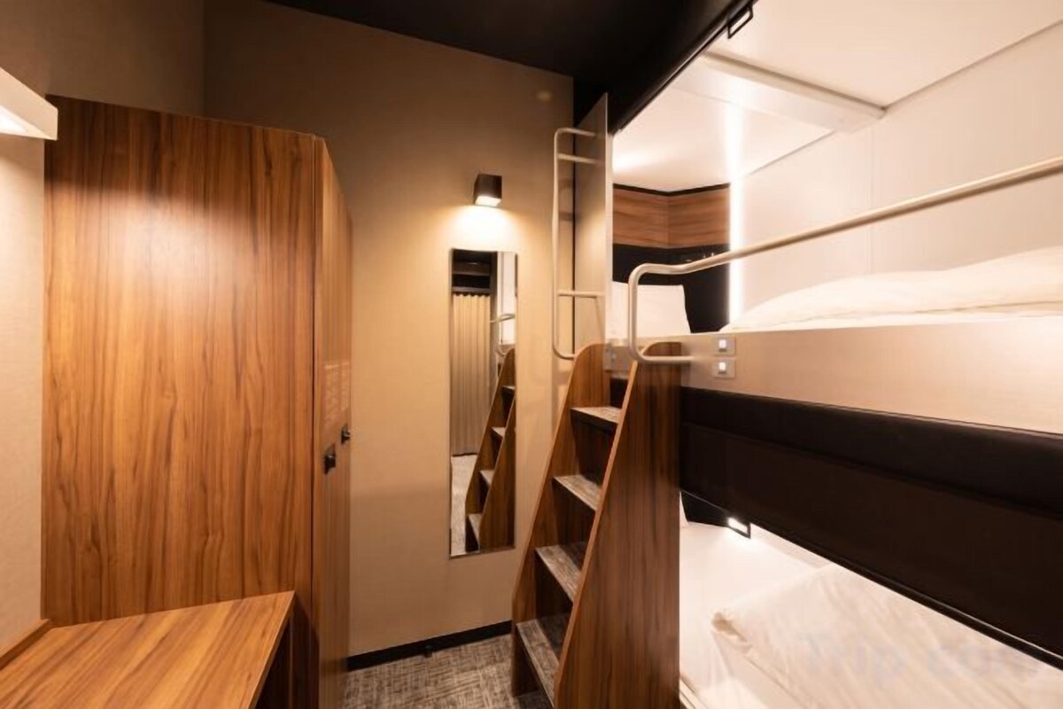 A compact hotel room with a wooden wardrobe, a small desk, a bunk bed, and a mirror.