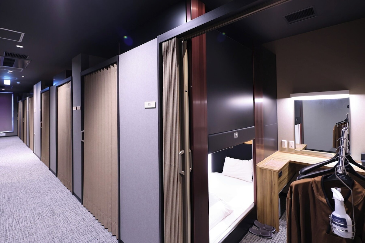 Habitación de hotel con cama, escritorio, espejo y zona de ducha.