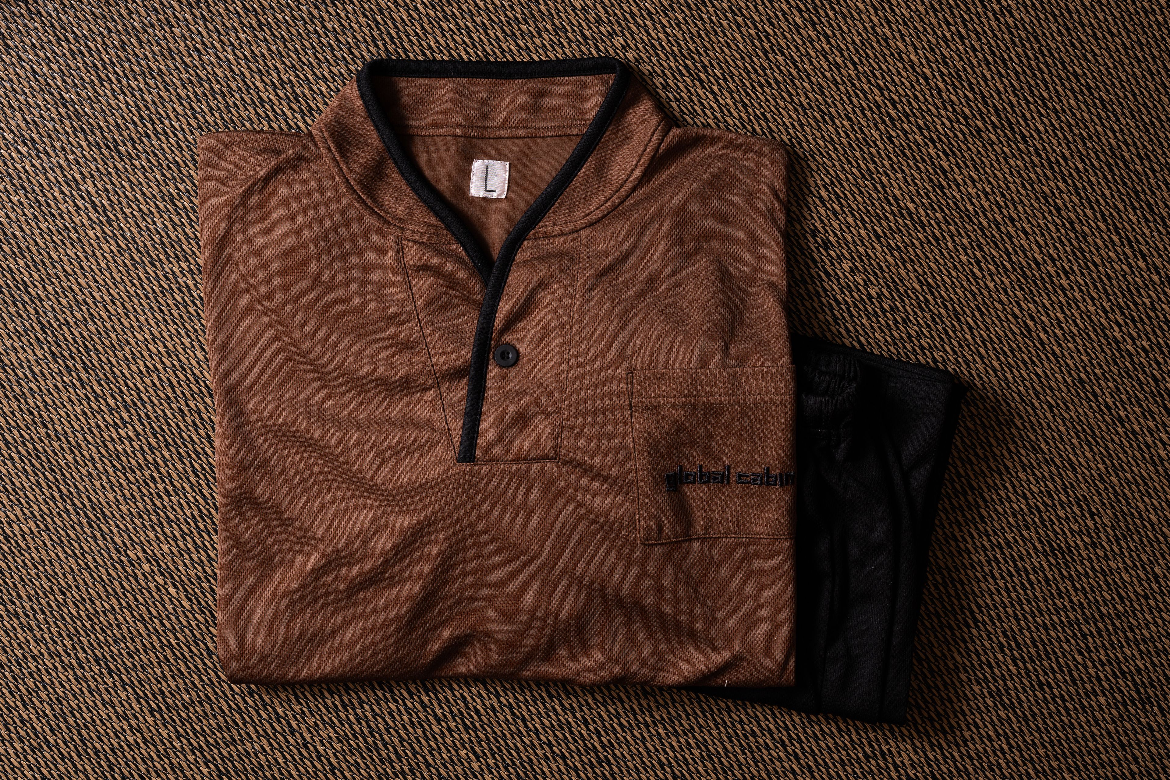 A brown shirt with a black collar and a pocket on the left side, placed on a woven surface.