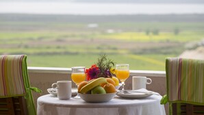 Une table avec un panier de fruits, deux verres de jus d’orange et une tasse, le tout placé devant un paysage pittoresque.