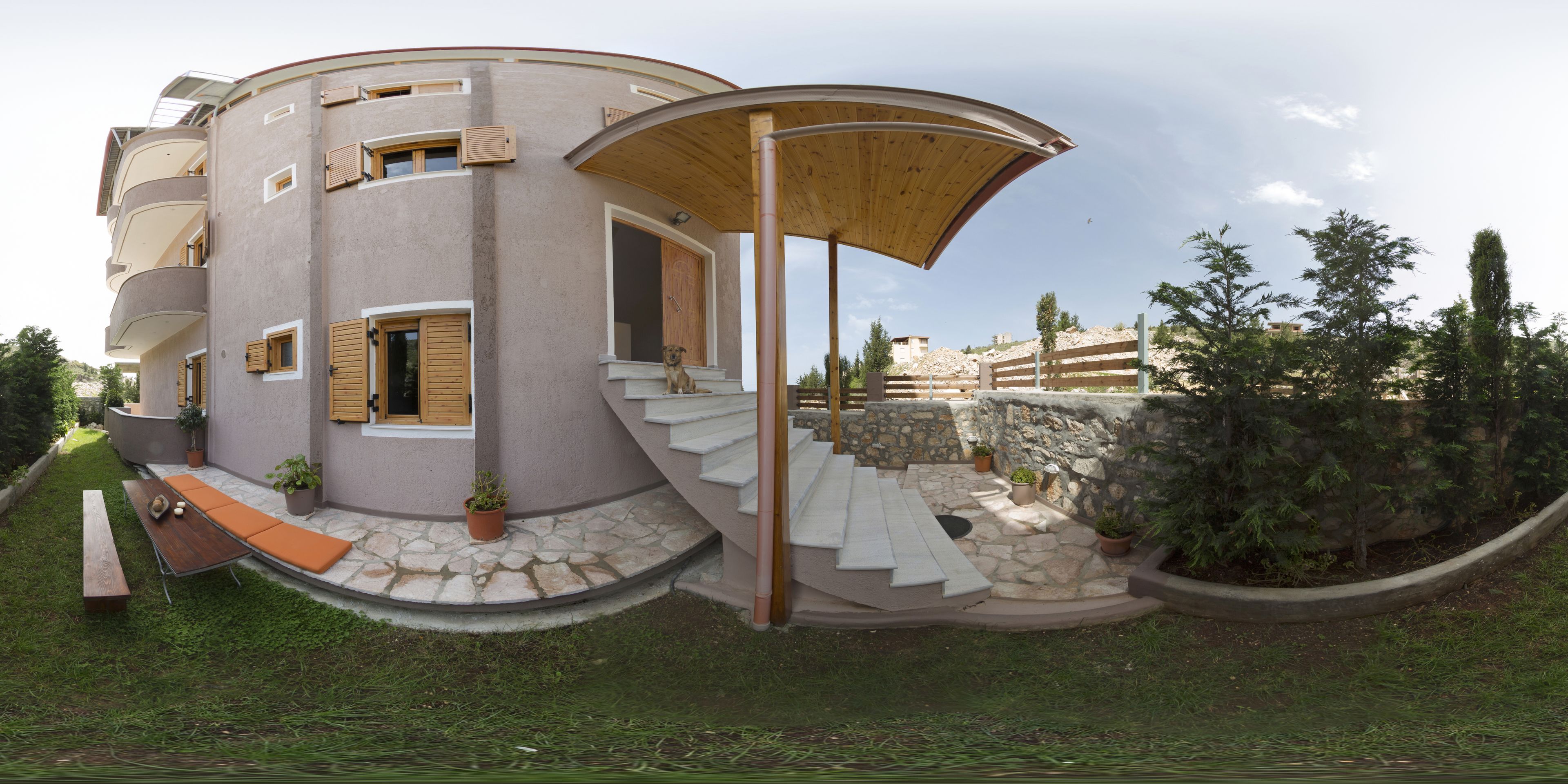 A modern, multi-level house with a curved exterior, a wooden staircase, and a covered outdoor seating area.