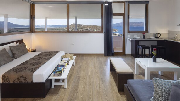 Une chambre d’hôtel moderne dotée d’un grand lit, d’un canapé, d’une petite table et offrant une vue sur la mer et les montagnes.
