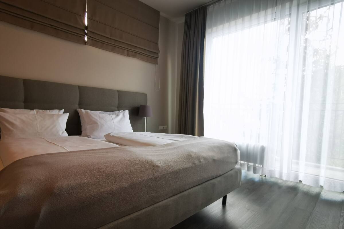 A large bed with a headboard, white bedding, and a lamp on a bedside table.