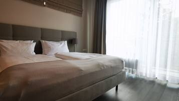 Una cama grande con cabecera, ropa blanca de cama y una lámpara en una mesita de noche.