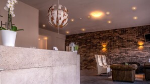 A modern interior with a brick wall, a concrete reception desk, a white chair, a brown sofa, and a unique spherical light fixture. - Hotel Gutsmühle (Obernburg)